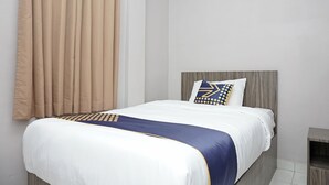Un lit bien fait, recouvert d’une couvre-lit blanche et bleue, avec une tête de lit en bois et un oreiller orné d’un motif géométrique.