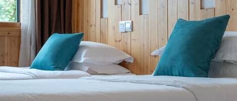 Habitación de hotel con cabecera de madera, ropa de cama blanca y almohadas azul turquesa.