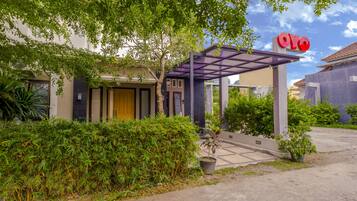 L’entrée d’un hôtel, avec un passage couvert, une enseigne indiquant « OYO » et un jardin bien entretenu.