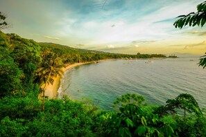 Paisagem costeira com praia, vegetação densa e céu claro.