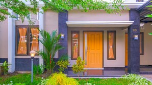 A modern building with a well-maintained garden, a wooden door, and a number E5 on the wall. - OYO 2284 Grand Villa Meninting (Senggigi)