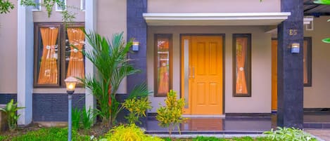 A modern building with a well-maintained garden, a wooden door, and a number E5 on the wall.