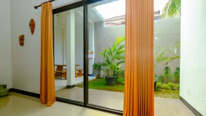 A room with a sliding glass door leading to a courtyard with plants and a small seating area. - OYO 2284 Grand Villa Meninting (Senggigi)