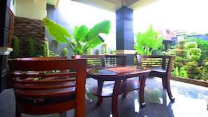 Un conjunto de banco y mesa de madera en un patio soleado, con vista a un jardín y un edificio al fondo.