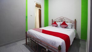 Una cama bien hecha con una colcha blanca y roja, un marco de cama de metal y una ventana con cortina marrón.
