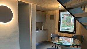A modern kitchen with a circular light feature, a dining area with a glass table, and a view of the outdoors through a window. - Retreat in Malcantone (Alto Malcantone)