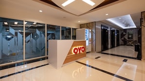 A modern reception area with a wooden reception desk labeled "OYO," glass walls, and a polished floor. - OYO 2245 Apartment Grand Kamala Lagoon (Bekasi)