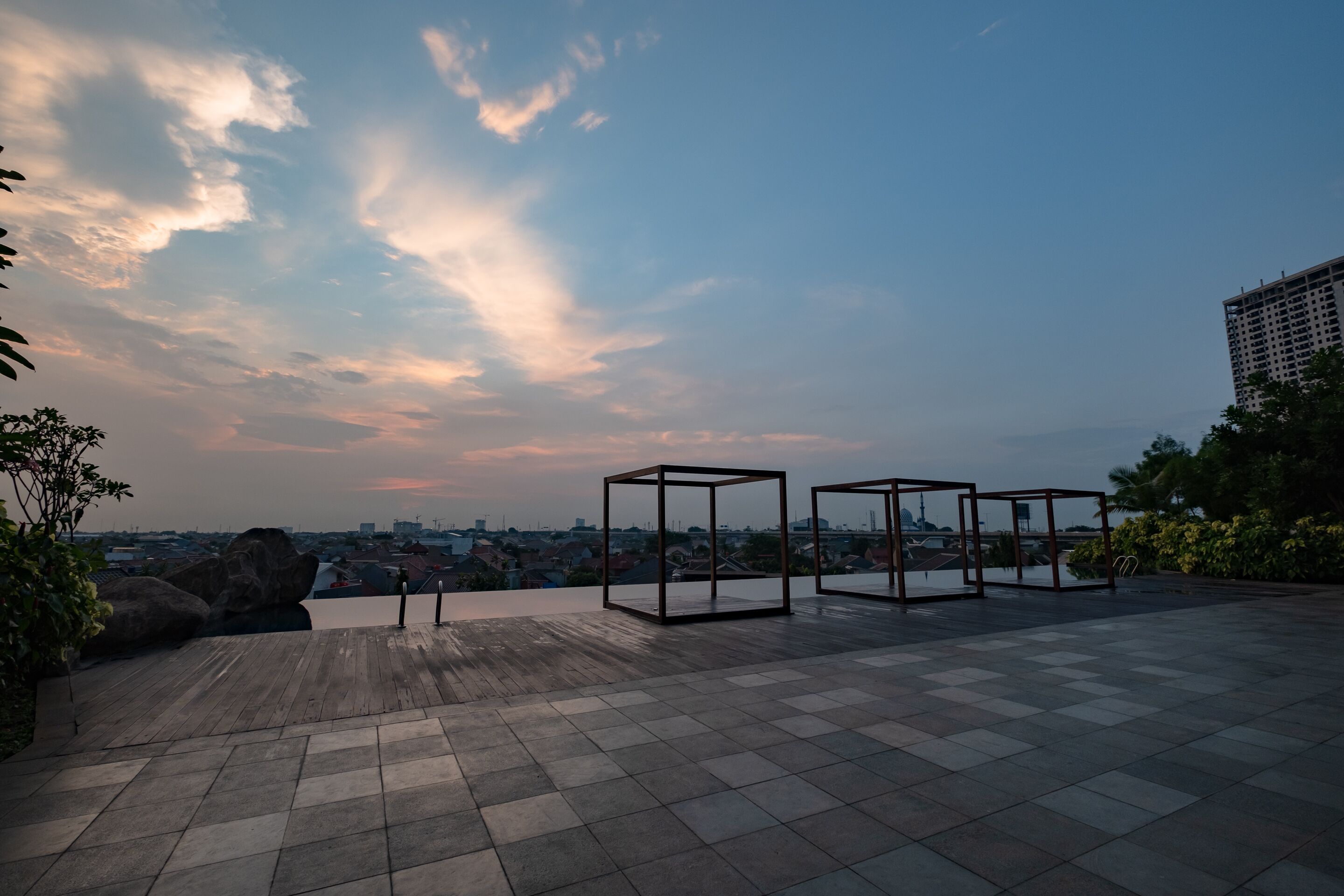 A rooftop terrace with a cityscape view, featuring a tiled floor and metal-framed structures.
