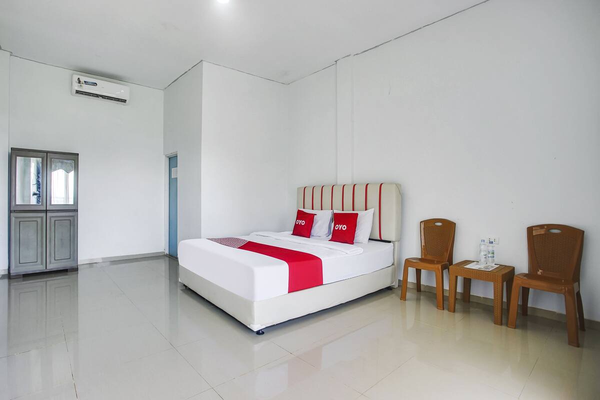 A hotel room with a bed, two wooden chairs, a small table, and a cabinet.
