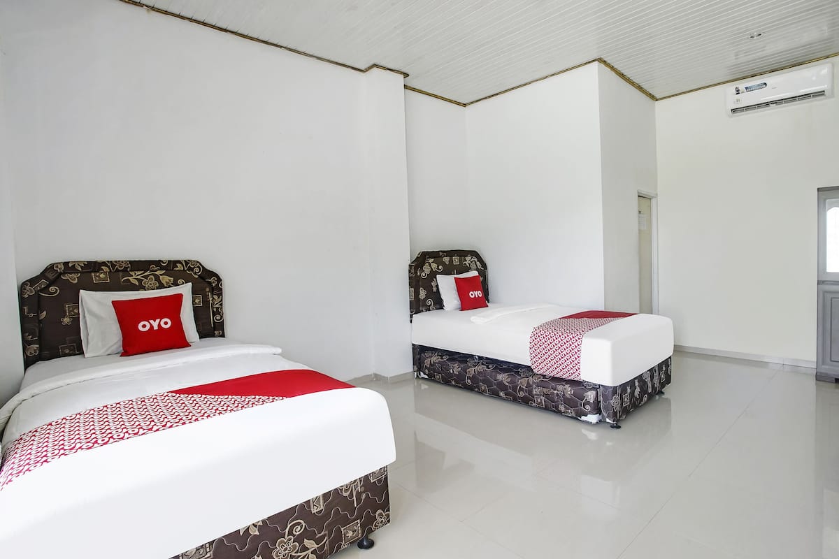 Two beds with patterned headboards, a red pillow with "OYO" text, and a white air conditioning unit on the wall.