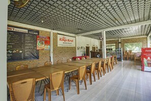 A restaurant with a long wooden table and wicker chairs, a menu board, and a sign for 'King's Kruis Hotel & Resort'. - OYO 2246 Anjung Bang Oking Hotel & Resort (Karya Penggawa)