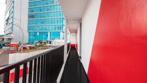 Un pasillo con pared roja y vista a un edificio moderno con ventanas azules.
