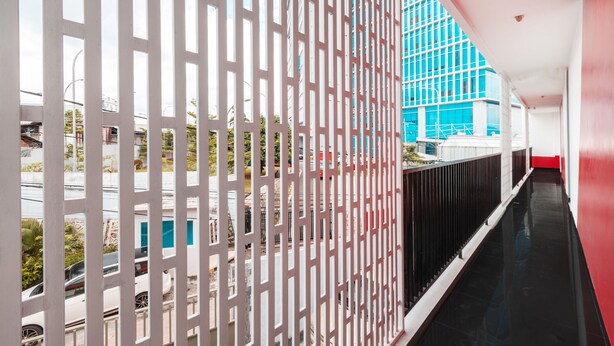 Un pasillo con una partición blanca, una barandilla negra y vista a un edificio azul.