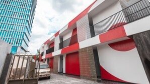 Un edificio de varios pisos con fachada roja y blanca, entrada protegida por una reja y un vehículo estacionado.