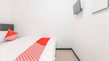 A hotel room with a bed, a red and white patterned bedspread, a grey headboard, a red pillow, a flat-screen TV mounted on the wall, and a white wall.