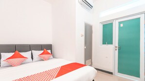 Una habitación de hotel con una cama, dos almohadas, una puerta verde y un equipo de aire acondicionado.