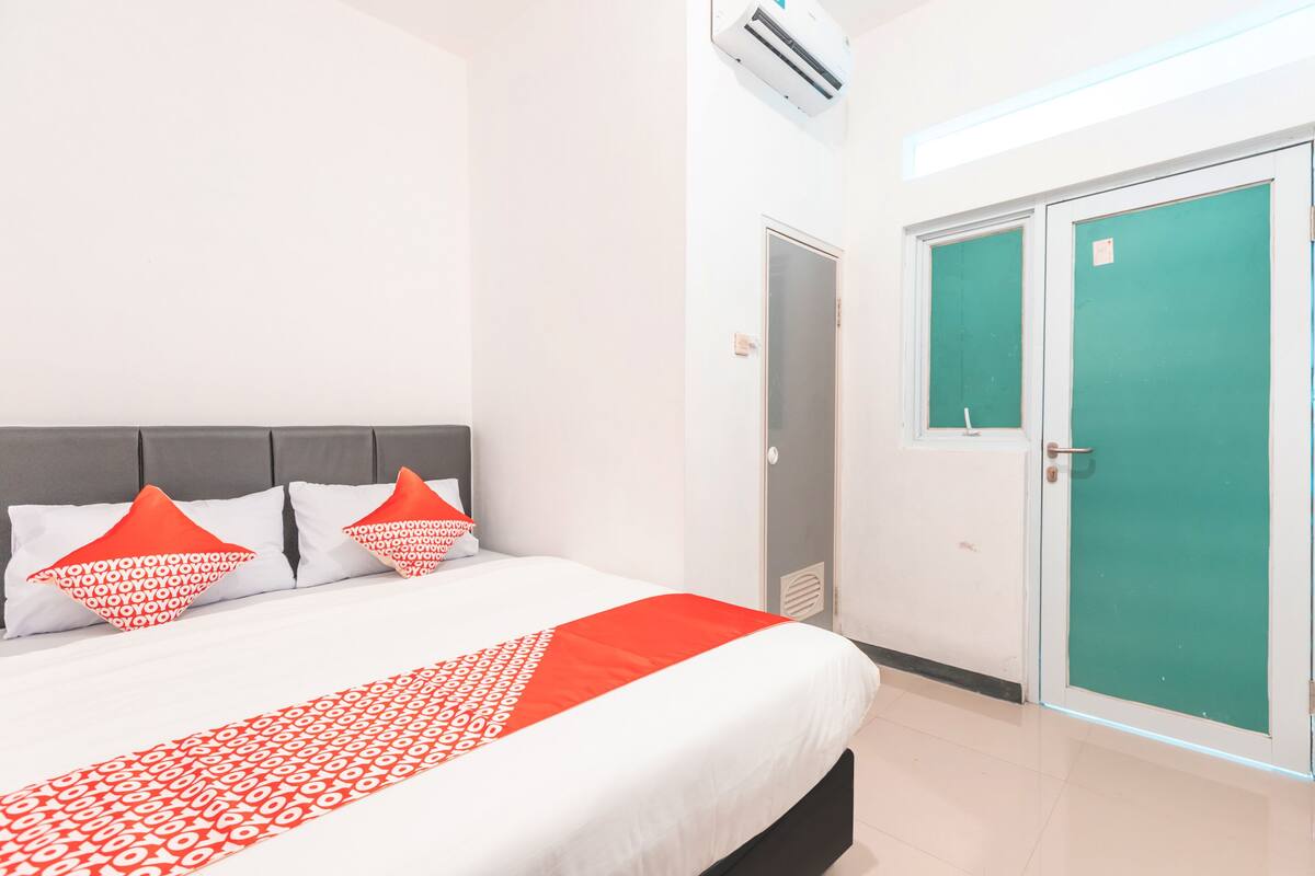 Une chambre d’hôtel avec un lit, deux oreillers, une porte verte et un appareil de climatisation.