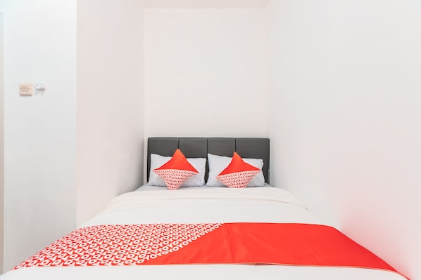 A bed with a grey headboard, white bedding, and red and white patterned pillows.