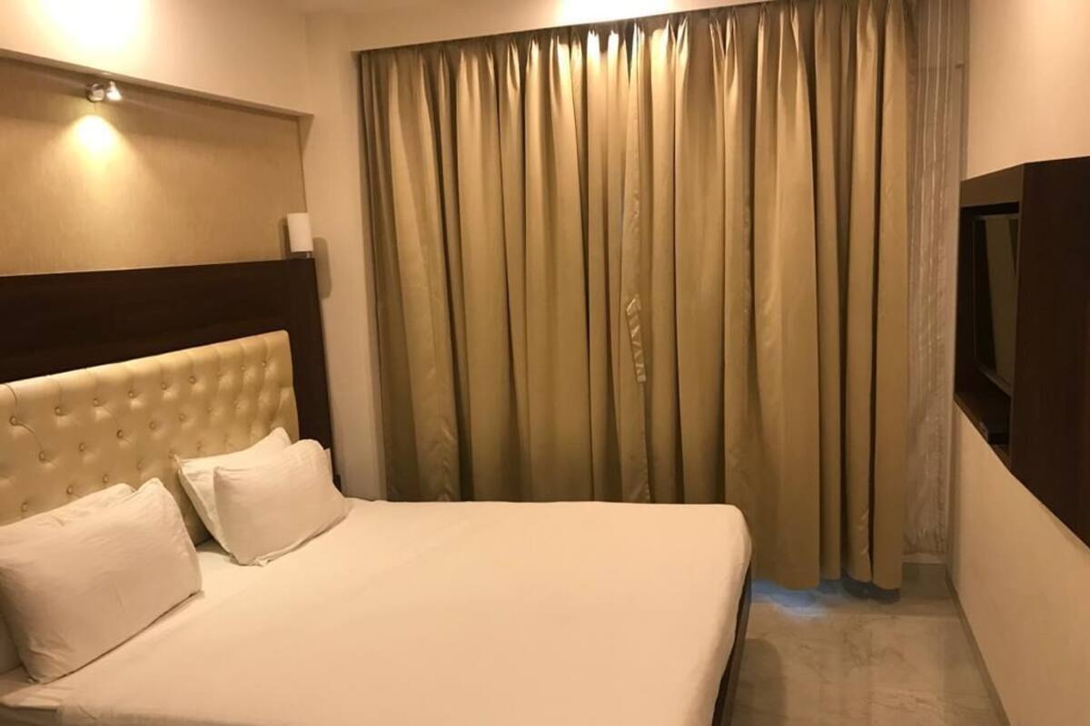 A hotel room with a large bed, a headboard, a flat-screen TV, and a curtain.
