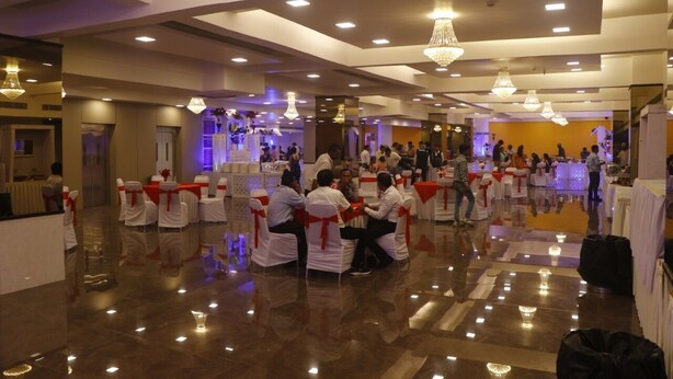 A spacious indoor event space with multiple round tables and chairs, chandeliers, and a polished floor. - Hotel Shivam (Kalyan)