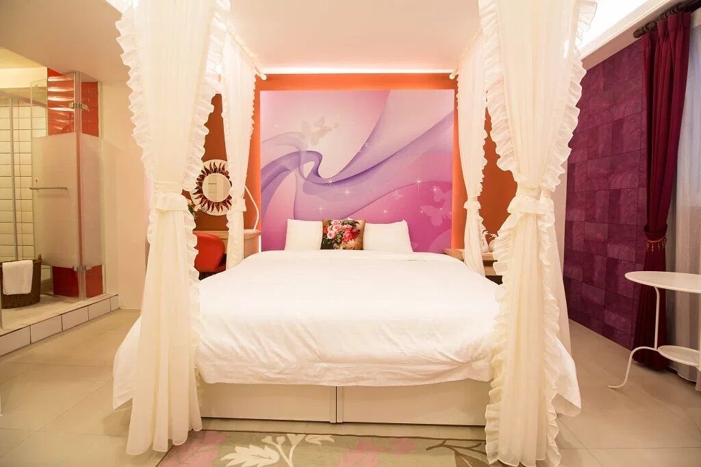 A bedroom with a canopy bed, a large wall mural, and a small table.