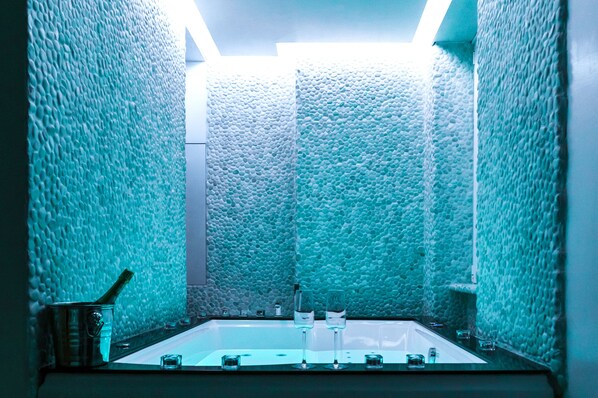Un baño con paredes texturizadas, una bañera y un lavabo con vasos y una botella.