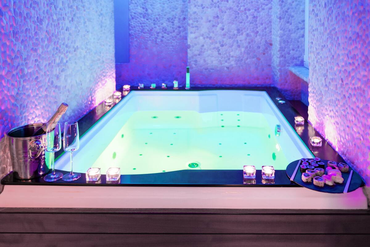 A spa tub with a stone wall backdrop, a bucket, glasses, and candles.