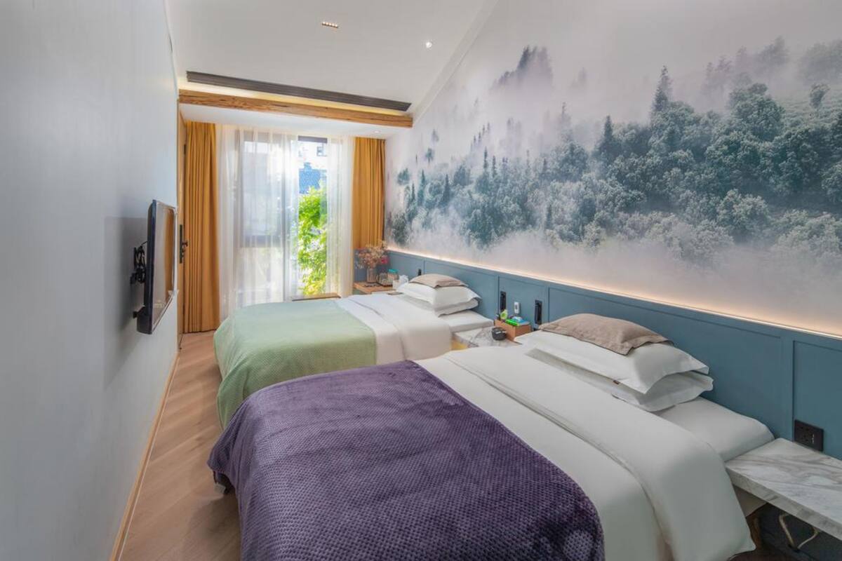 Ein Hotelzimmer mit zwei Betten, einer großen Wandmalerei und einer Glastür, die auf einen Balkon führt.
