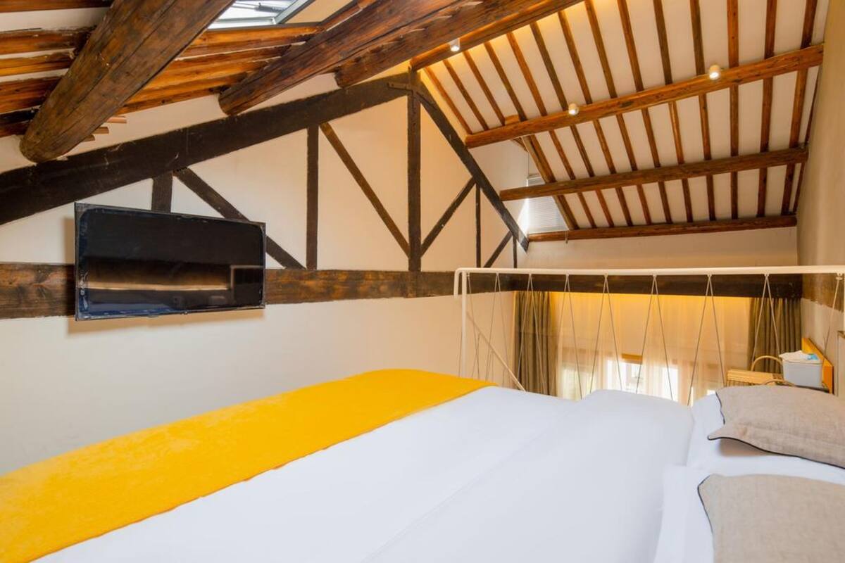Ein Schlafzimmer mit einem Bett, einem an der Wand montierten Fernseher und einer schrägen Decke mit Holzbalken.