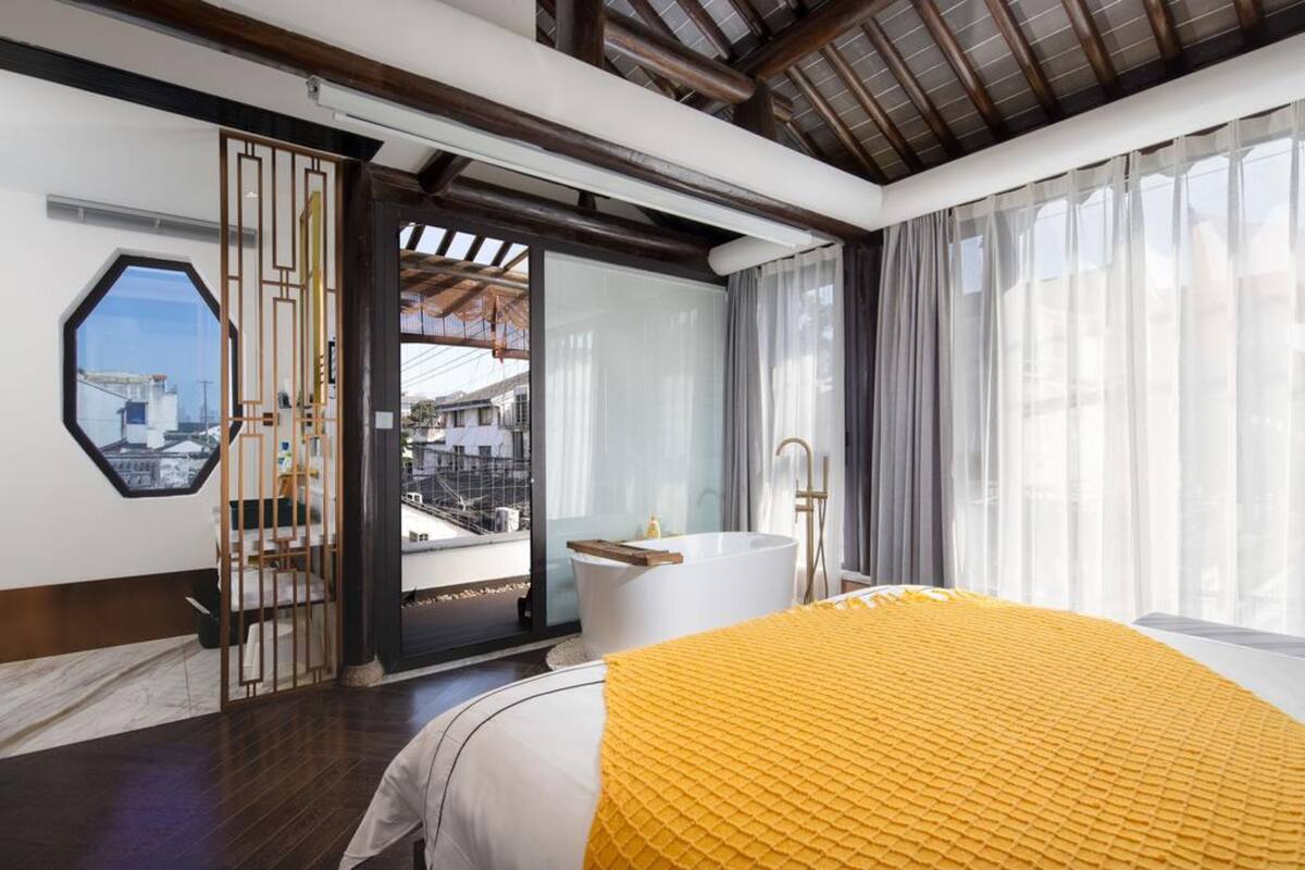 Ein modernes Hotelzimmer mit einem großen Bett, einer Badewanne und Blick auf die Stadt durch ein großes Fenster.
