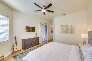Une chambre à coucher avec un lit, une commode, un téléviseur, une guitare et un ventilateur de plafond.