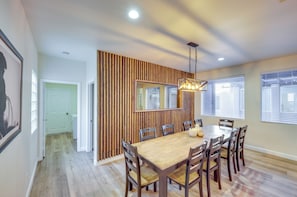 Un coin repas avec une table et des chaises en bois, un luminaire suspendu et un grand miroir au mur.