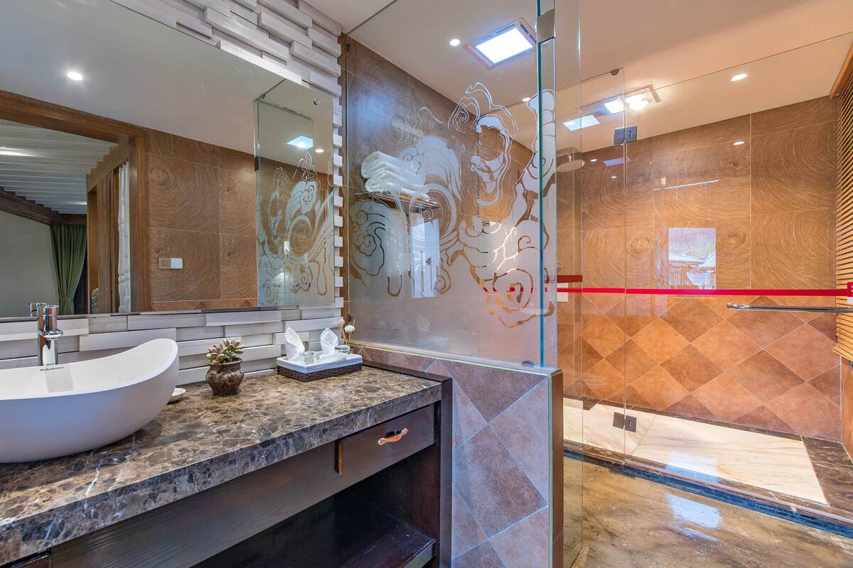 A modern bathroom with a large white vessel sink, a glass shower enclosure, and a marble countertop.