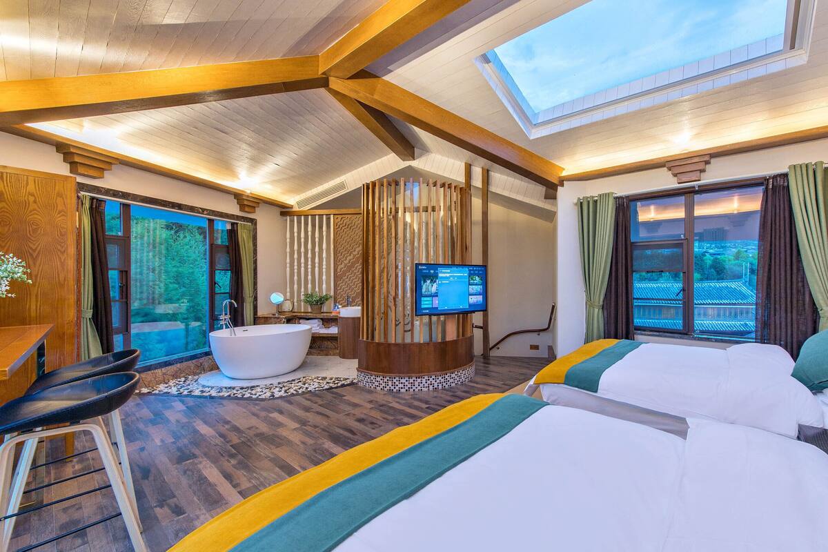 A modern hotel room with a large skylight, a bathtub, a television, and a bed with colorful bedding.