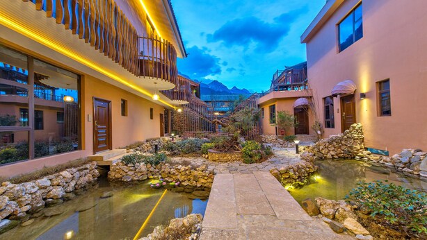 A courtyard with a stone pathway leading to a water feature surrounded by plants and rocks. - Floral Hotel Yun Shui Snow Mountain (Lijiang)