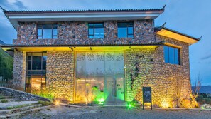 Un edificio de piedra con techo tradicional, una entrada amplia con celosía decorativa y un cartel que indica un sendero de montaña.