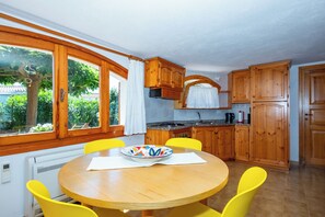Une cuisine avec des meubles en bois, une table ronde entourée de chaises jaunes et une fenêtre donnant sur un paysage verdoyant.