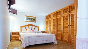 Een slaapkamer met een houten bed, nachtkastje, kledingkast en een schilderij aan de muur.