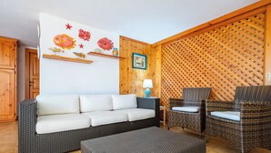 Een kamer met een grijze bank, rieten stoelen, een kleine tafel met een lamp, houten wanden en een decoratie aan de muur met een vis thema.