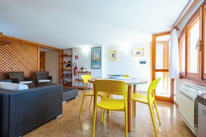 Un salon avec un canapé, des fauteuils jaunes, une table à manger et un coin cuisine avec une fenêtre.