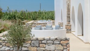 A stone-walled outdoor seating area with white cushions and a view of the sea.