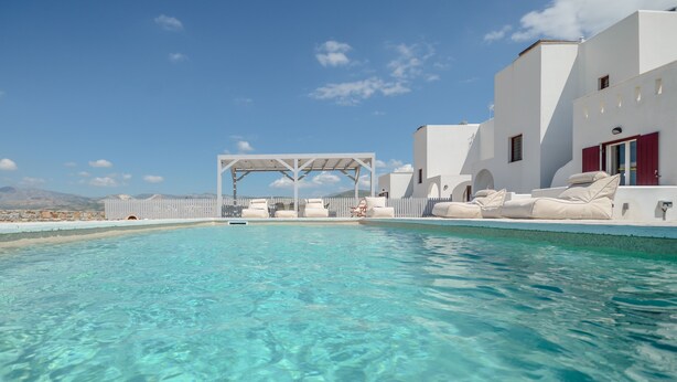A clear blue pool with white buildings and red shutters in the background.