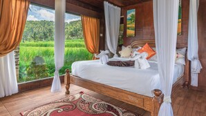 Un letto a baldacchino in legno con lenzuola bianche, un tappeto rosso con motivi e vista su un paesaggio verdeggiante.