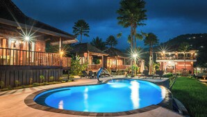 Una piscina circondata da edifici in legno con zone relax all'aperto e un patio ben illuminato.