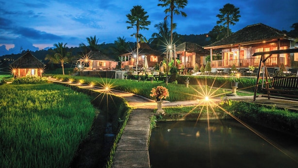 Un resort ben illuminato con diversi edifici, un canale d'acqua e una vegetazione lussureggiante.