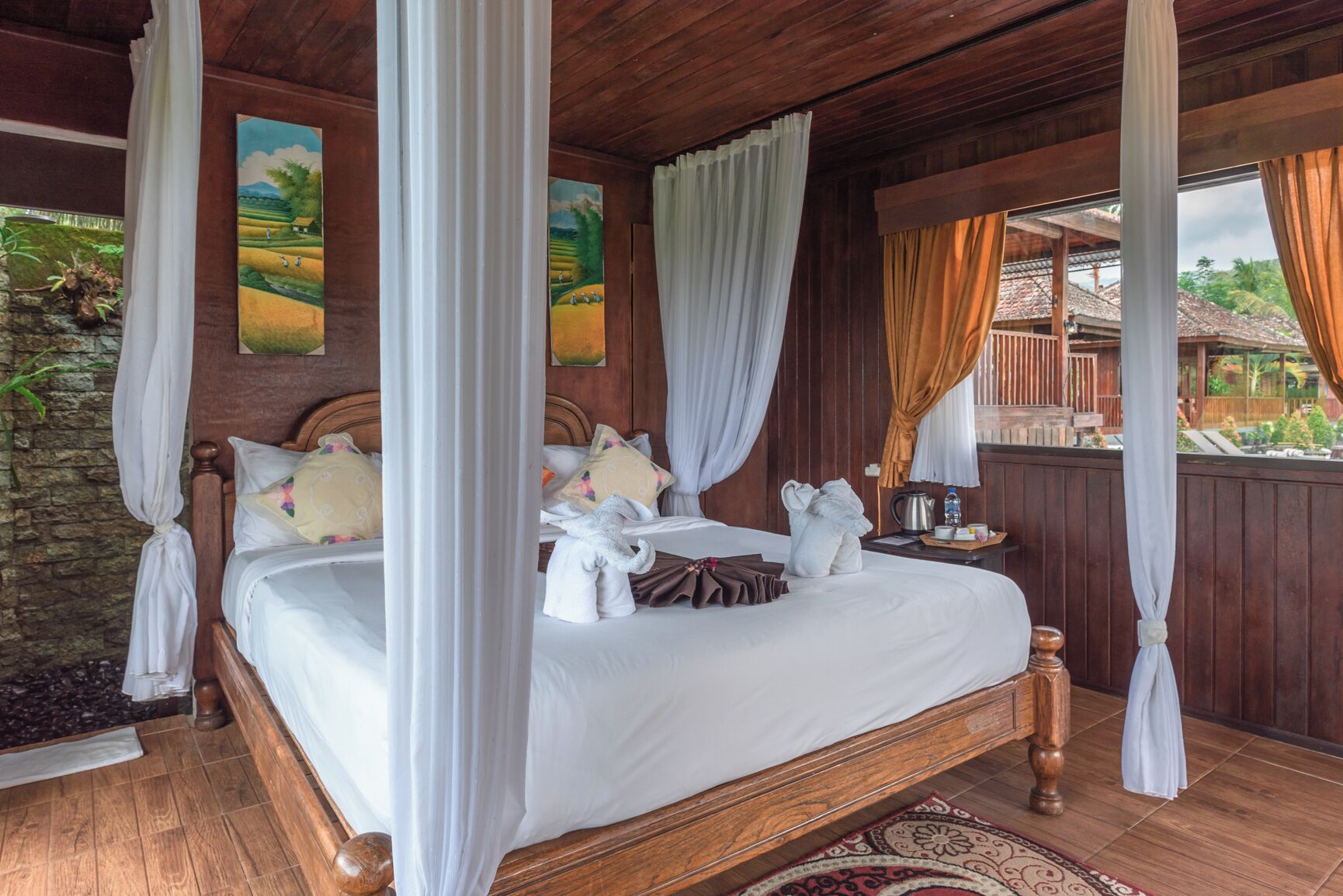 A four-poster bed with white linens, wooden headboard, and a nightstand with a kettle and water bottle.