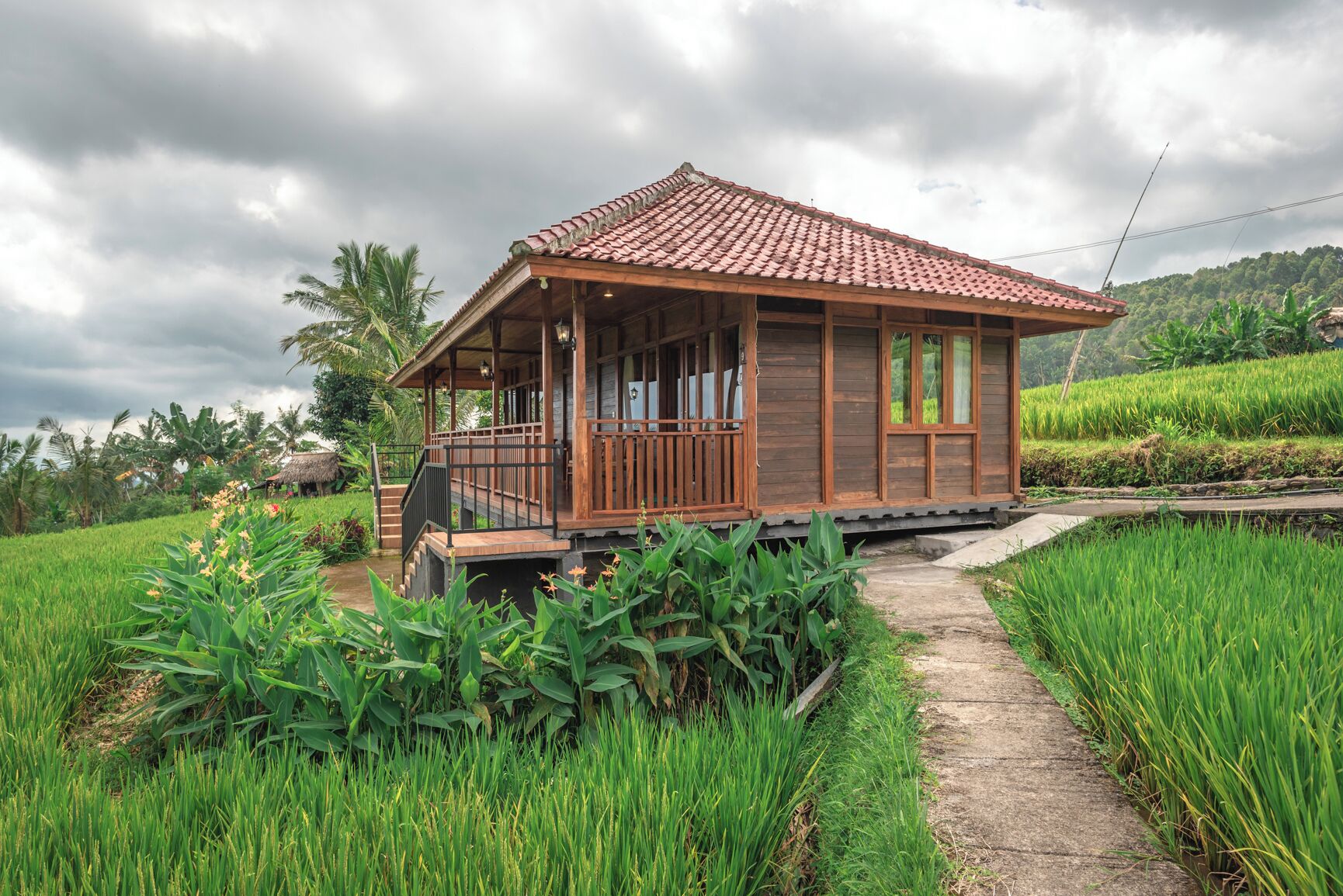 A wooden house with a tiled roof, surrounded by lush green fields and a clear sky.