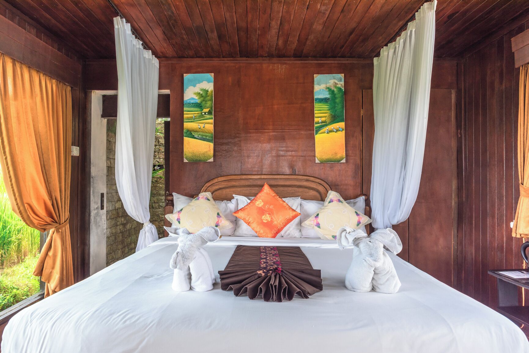 A wooden room with a bed, curtains, and two paintings on the wall.