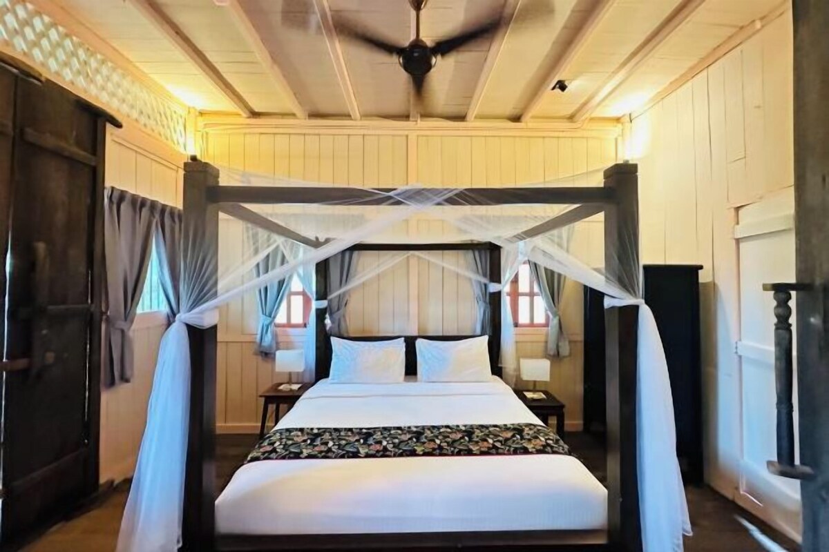 A four-poster bed with a canopy, a ceiling fan, and a nightstand with a lamp.