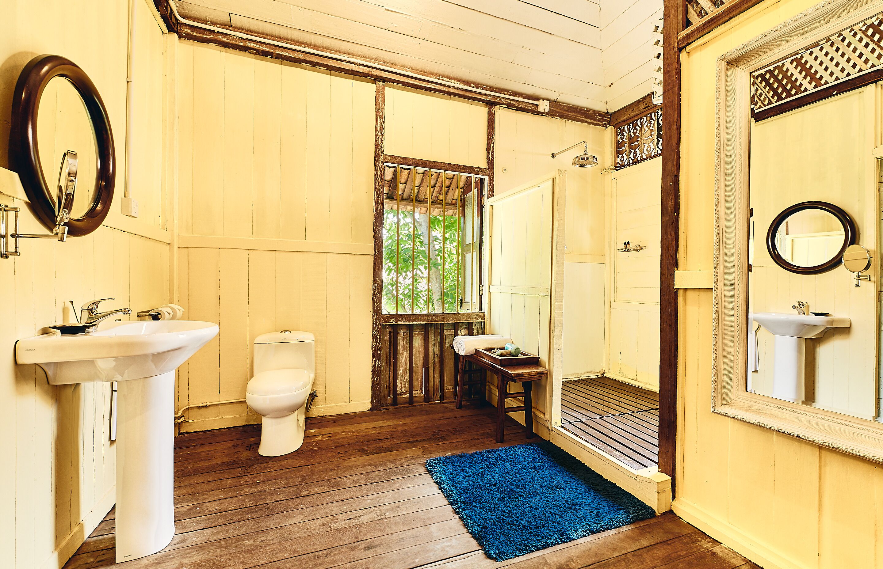 A bathroom with wooden floors, a white sink, a toilet, and a shower area.